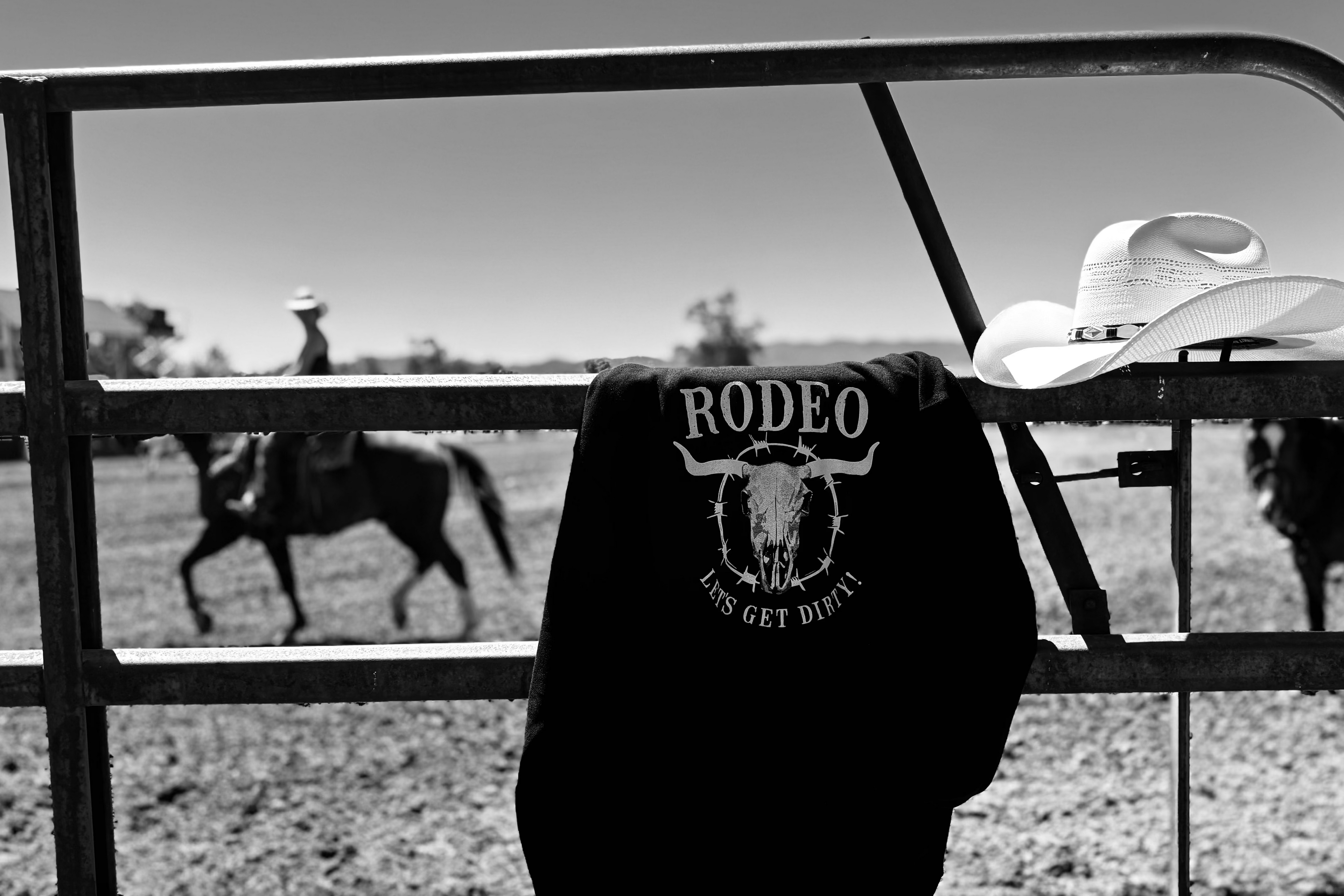 Rodeo shirt with a cowboy hat on a fence in a field with people on horses in the background.